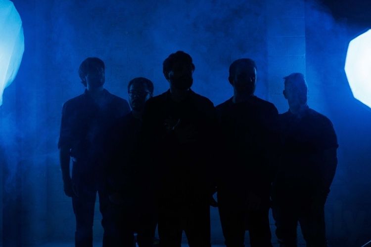 Absent Theory in silhouette, lit from behind through heavy fog